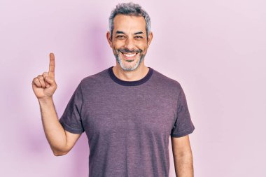 Yakışıklı, orta yaşlı, gri saçlı, işaret parmağıyla işaret eden mutlu ve havalı bir gülümsemeyle gülümseyen bir adam. diş gösterme. 