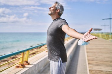 Middle age hispanic man wearing sportswear breathing at seaside