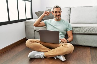 Orta yaşlı İspanyol bir adam oturma odasında dizüstü bilgisayar kullanıyor. Gülümsüyor ve tek parmağıyla kafasını işaret ediyor. Harika bir fikir ya da düşünce, iyi bir hafıza. 