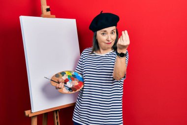 Orta yaşlı İspanyol kadın paletle resim çiziyor. Resim sehpası ayakta duruyor. İtalyan jestleri yapıyor. 