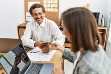Orta yaşlı erkek ve kadın işçiler ofiste dizüstü bilgisayar kullanarak dolar ödüyorlar.