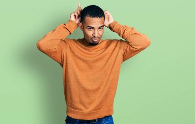 Genç, Afro-Amerikan bir adam, günlük kıyafetler giyip, boynuzları üzerinde parmaklarıyla komik jestler yapıyor. 