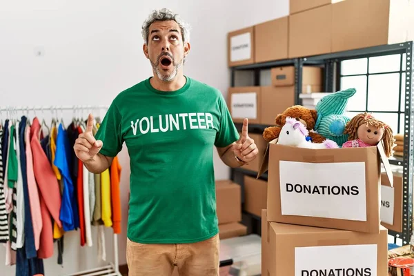 Bağışta gönüllü tişört giyen orta yaşlı İspanyol adam şaşırmış ve şaşırmış bir şekilde başını kaldırıp parmaklarıyla işaret ediyor ve kollarını kaldırıyordu.. 