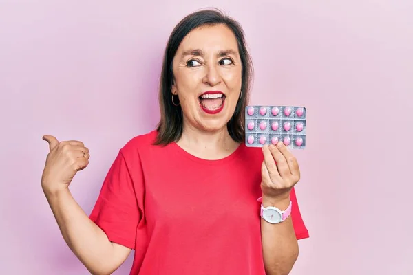 Middle Age Hispanic Woman Holding Pills Pointing Thumb Side Smiling — Stock fotografie