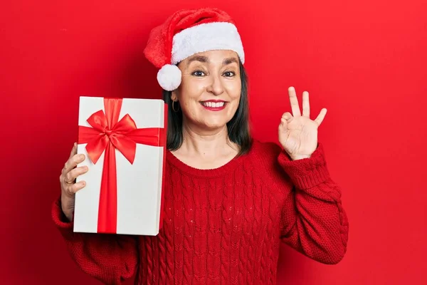 Middle Age Hispanic Woman Wearing Christmas Hat Holding Gift Doing — стоковое фото