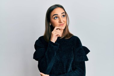 Young brunette girl wearing elegant fashion sweater thinking concentrated about doubt with finger on chin and looking up wondering 