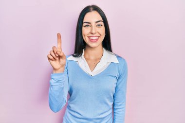 Pembe arka planda duran mavi gözlü güzel bir kadın bir numarayı gösterip işaret ederken kendinden emin ve mutlu bir şekilde gülümsüyor.. 