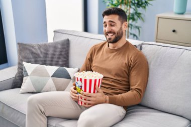 Evdeki kanepede oturmuş film izleyen İspanyol genç adam.