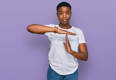 Young african american woman wearing casual white t shirt doing time out gesture with hands, frustrated and serious face  clipart