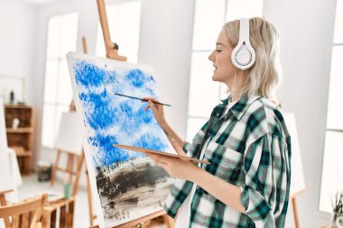 Sanat stüdyosunda resim yaparken ve müzik dinlerken gülümseyen genç sanatçı kız..