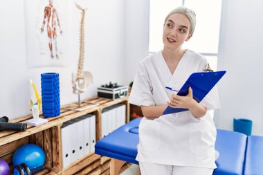 Klinikte çalışan, fizyoterapist üniforması giyen beyaz bir kadın.