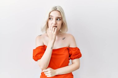 Tecrit edilmiş arka planda duran genç beyaz kadın elleri ağızda tırnak yerken gergin ve stresli görünüyor. anksiyete. 