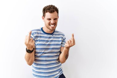 Handsome young man standing over isolated background showing middle finger doing fuck you bad expression, provocation and rude attitude. screaming excited 