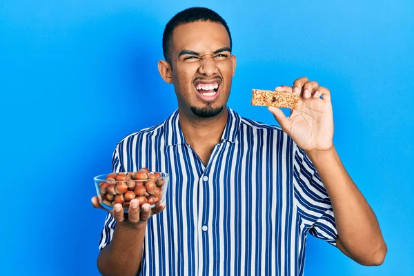 Joven Hombre Afroamericano Sosteniendo Avellanas Crudas Barra Cereal Enojado Loco — Foto de Stock