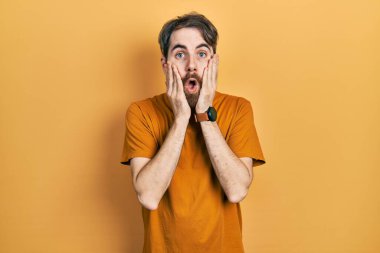 Sakallı, sıradan sarı tişörtlü beyaz bir adam. Korkmuş ve şok olmuş. Şaşırmış ve şaşırmış. 