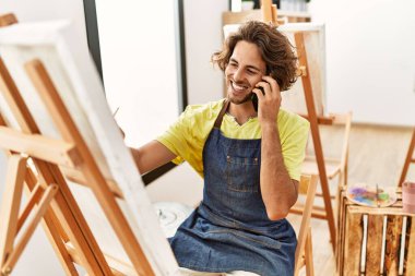 Genç İspanyol sanatçı gülümsüyor mutlu çizimler yapıyor ve resim stüdyosundaki akıllı telefondan konuşuyor..