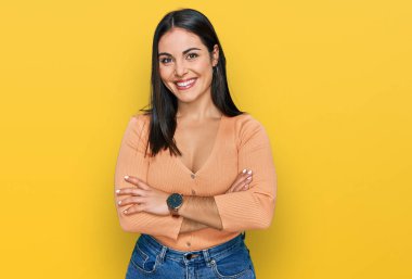 Gündelik kıyafetler giyen, kollarını kavuşturup kameraya gülümseyen genç İspanyol kadın. pozitif kişi. 