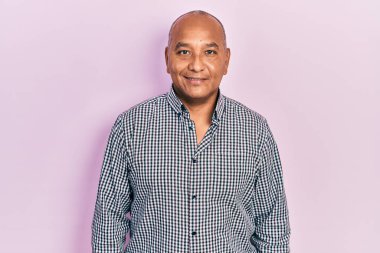 Yüzünde mutlu ve havalı bir gülümseme olan gündelik kıyafetler giyen orta yaşlı Latin bir adam. şanslı kişi. 