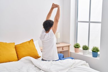 Young arab man waking up stretching arms at bedroom