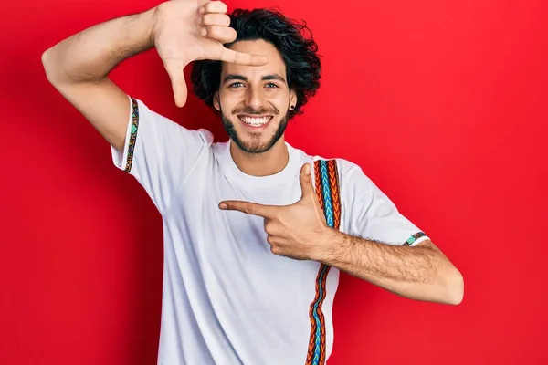 カジュアルな白いTシャツを着たハンサムなヒスパニック系の男性は 幸せな顔をした手と指でフレームを作り笑顔 創造性と写真の概念 — ストック写真