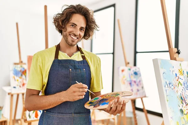 在艺术工作室拿着画笔和调色板时 他那年轻的惊慌失措的艺术家高兴地微笑着 — 图库照片