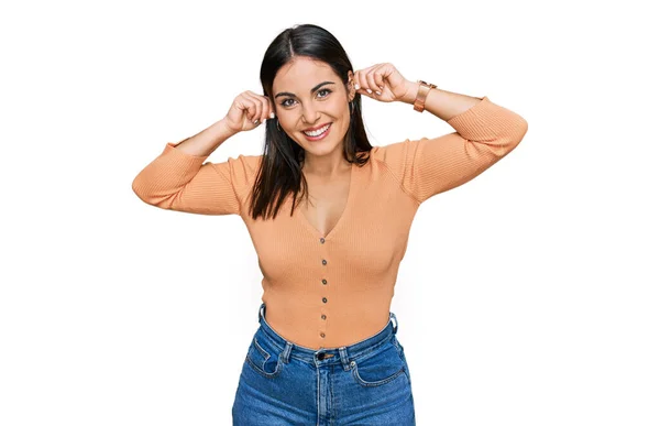 若いヒスパニック系の女性の指で耳を引く笑みを浮かべてカジュアルな服を着て 面白いジェスチャー オーディション問題 — ストック写真