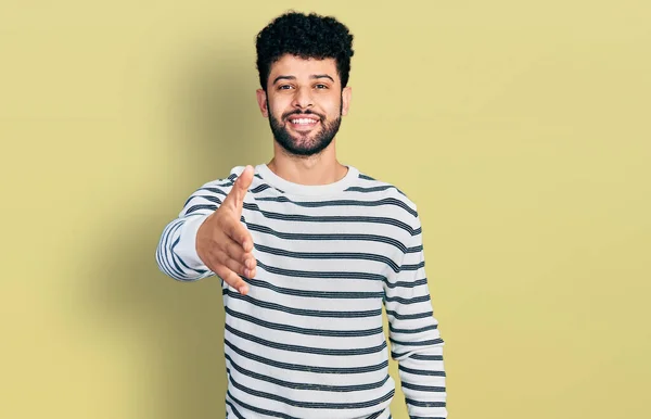 年轻的阿拉伯男子 留着胡子 身穿休闲条纹毛衣 微笑友好地握手致意和欢迎 成功的商业 — 图库照片