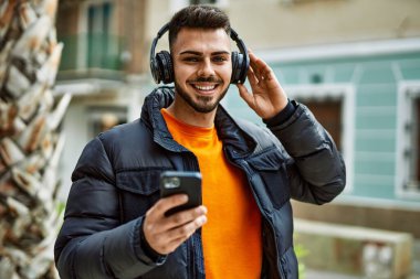 Yakışıklı, sakallı, neşeli, kendine güvenen, kışlık palto giyen, akıllı telefondan müzik dinleyen bir İspanyol.