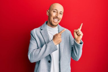 Sakallı, iş ceketi giyen, gülümseyen ve kameraya bakan kel bir adam.. 