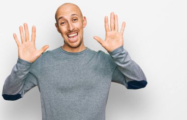 Kel, sakallı, günlük giysiler giymiş on numaralı parmaklarıyla onu gösterirken kendinden emin ve mutlu bir şekilde gülümsüyor.. 