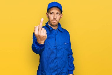Bald man with beard wearing builder jumpsuit uniform showing middle finger, impolite and rude fuck off expression 