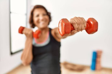 Orta yaşlı İspanyol sporcu kadın spor merkezinde dambıllar kullanarak mutlu bir antrenman yapıyor..