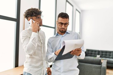 İki İspanyol iş adamı belge okuyor ve ofiste çalışan akıllı telefondan konuşuyor.