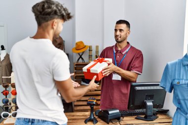 Genç İspanyol esnaf gülümseyerek giyim mağazasındaki müşteriye hediye veriyor..