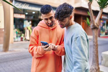 İki erkek caddede birbirlerine akıllı telefon kullanarak sarılıyorlar.