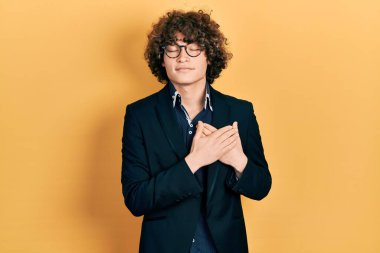 İş ceketi giyen, gözlüklü, göğsünde elleri kapalı, yüzünde minnet ifadesi olan yakışıklı bir genç. sağlık kavramı. 