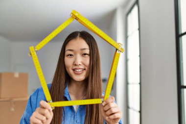 Genç Çinli kız mutlu bir şekilde gülümsüyor. Ev projesini ayakta tutuyor.