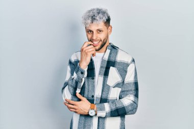 Modern boyalı saçlı, rahat gömlekli genç İspanyol adam kameraya kendinden emin, kollarını kavuşturmuş ve çenesini kaldırmış gülümsüyor. Olumlu düşünmek. 