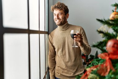 Genç İspanyol adam evde Noel ağacının yanında şarap içiyor.
