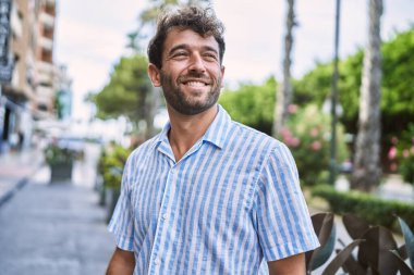 Genç İspanyol adam gülümseyerek şehirde mutlu mesut dikiliyor..