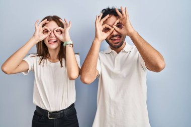 Genç bir çift, günlük giysiler giyip yan yana dururlar. Dürbün gibi jest yaparlar, gözleri parmaklarından dışarı bakar. çılgın ifade. 