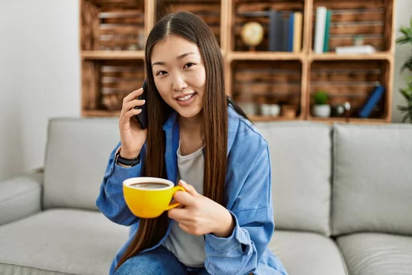 Ung Kinesisk Flicka Talar Smartphone Och Dricka Kaffe Sitter Soffan — Stockfoto