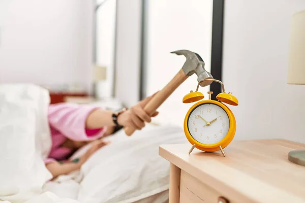女孩躺在床上用锤子关掉了卧室的闹钟 — 图库照片