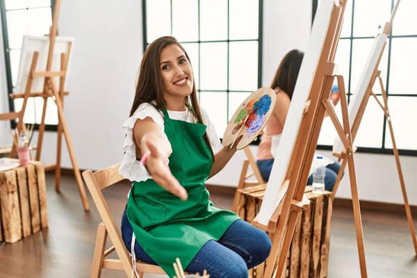若いヒスパニック系のアーティストの女性は 挨拶や歓迎として握手を提供フレンドリーな笑みを浮かべてアートスタジオでキャンバス上に絵を描く 成功したビジネス — ストック写真