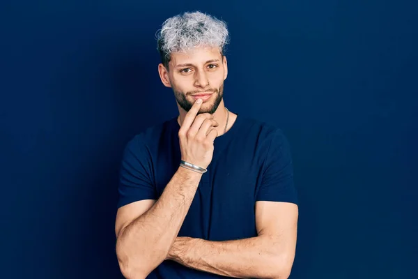 Young hispanic man with modern dyed hair wearing casual blue t shirt smiling looking confident at the camera with crossed arms and hand on chin. thinking positive.