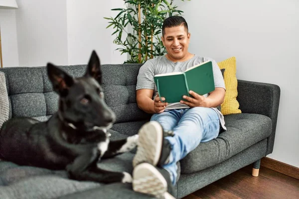 Jovem Hispânico Ler Livro Sentado Sofá Com Cão Casa — Fotografia de Stock
