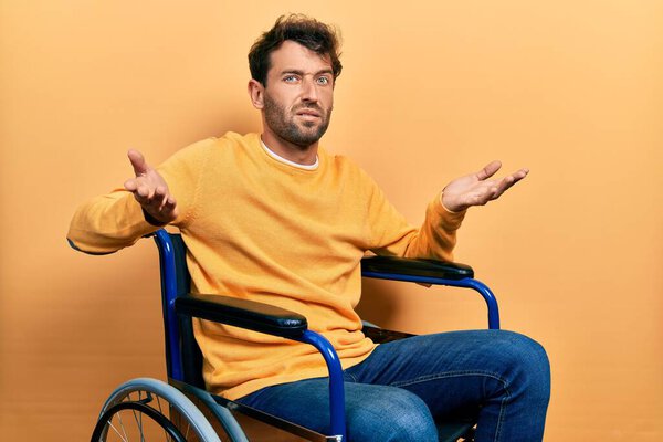 Handsome man with beard sitting on wheelchair clueless and confused with open arms, no idea concept. 