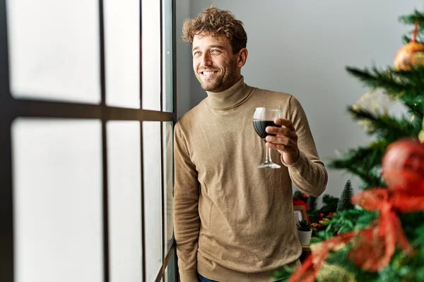 Genç İspanyol adam evde Noel ağacının yanında şarap içiyor.