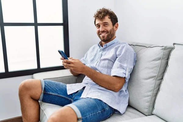 年轻的他的惊慌失措的男人坐在家里沙发上用智能手机 — 图库照片