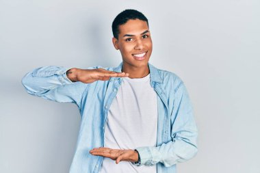 Young african american guy wearing casual clothes gesturing with hands showing big and large size sign, measure symbol. smiling looking at the camera. measuring concept. 